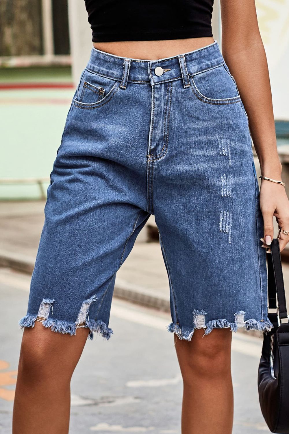 Medium wash denim bermuda shorts with frayed hem and distressed details.