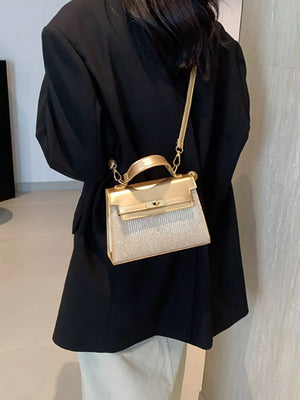 Gold glitter textured mini crossbody bag with top handle and strap.