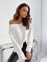 White off-shoulder knit top with gold buckle detail on strap and button cuffs.