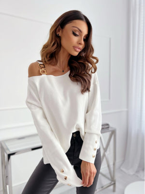 White off-shoulder knit top with gold buckle detail on strap and button cuffs.