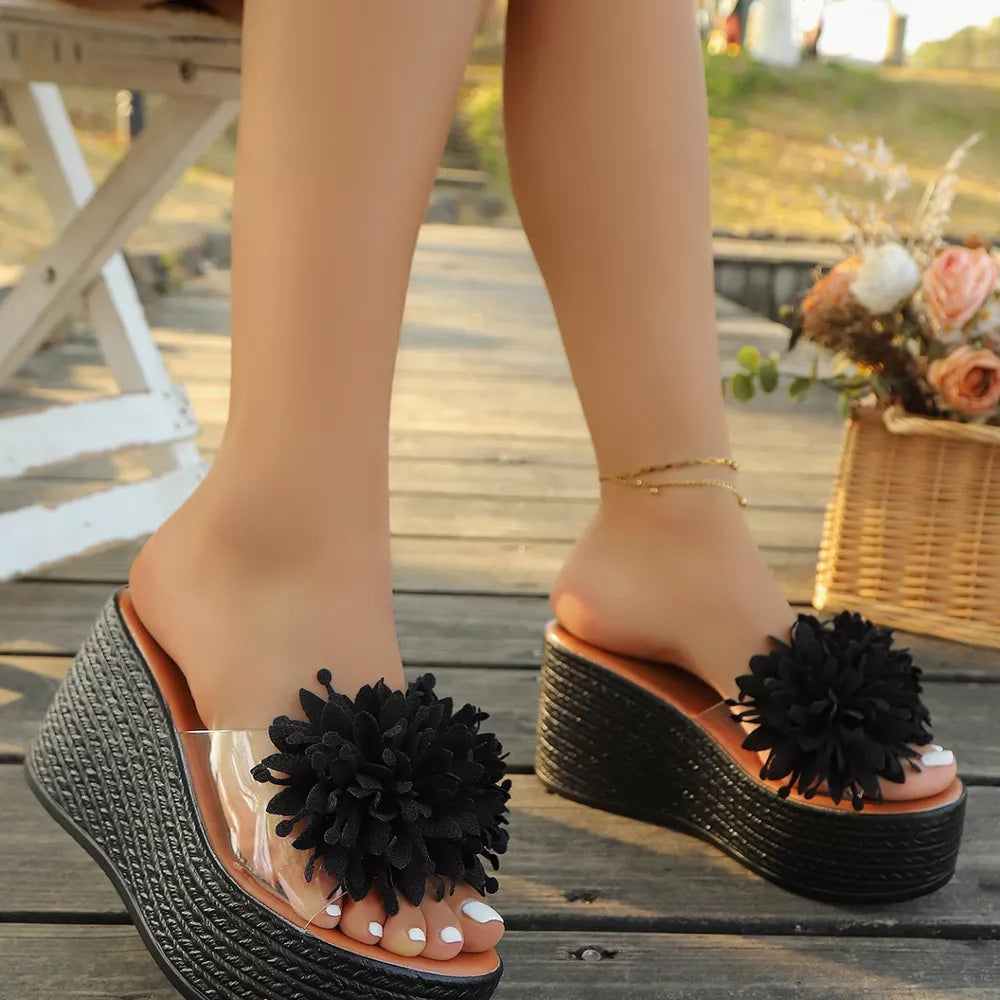 Black floral pom-pom wedge sandals with clear straps and braided espadrille wedge.