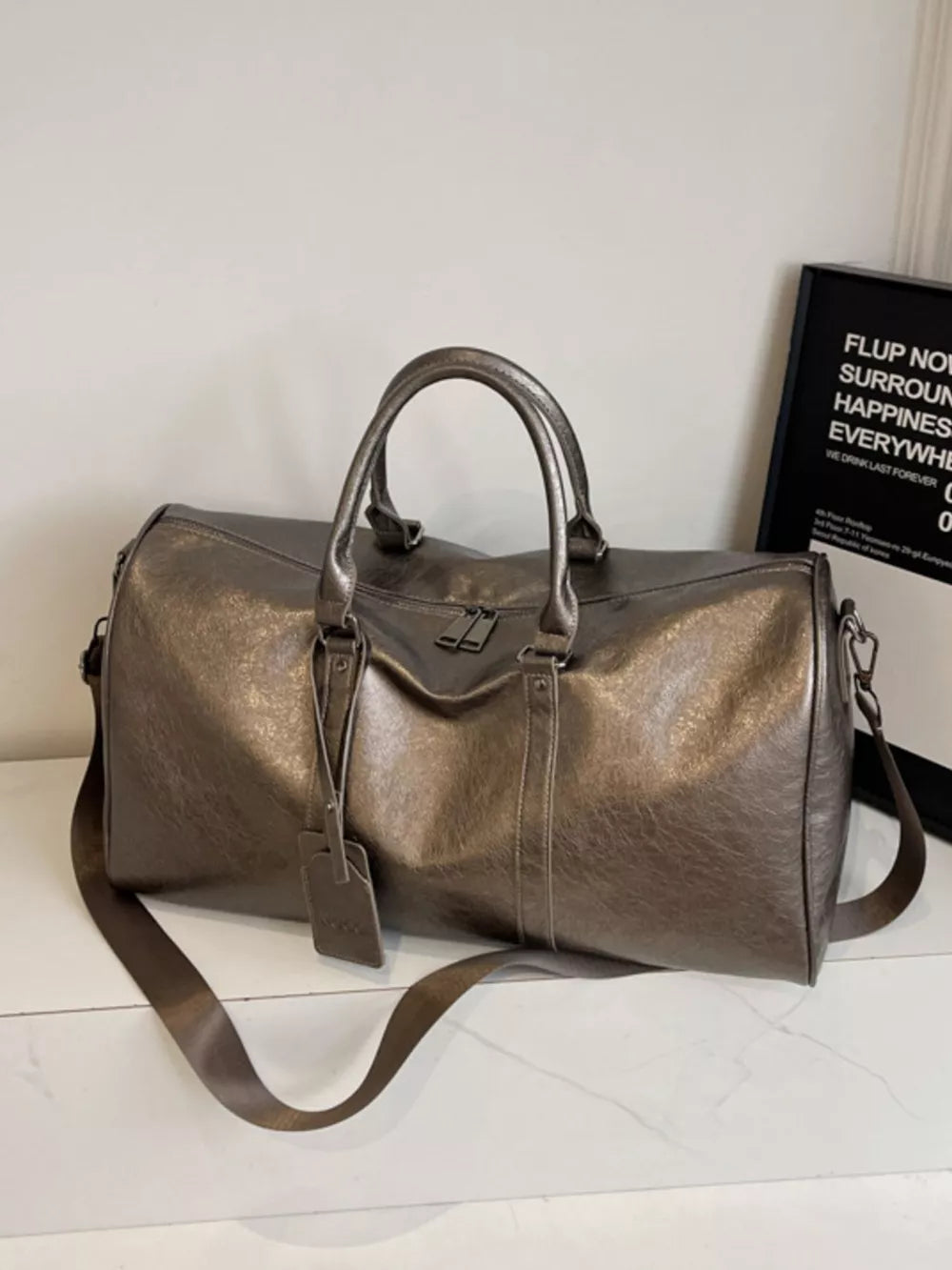 Textured metallic duffle bag in champagne color with detachable strap and luggage tag.