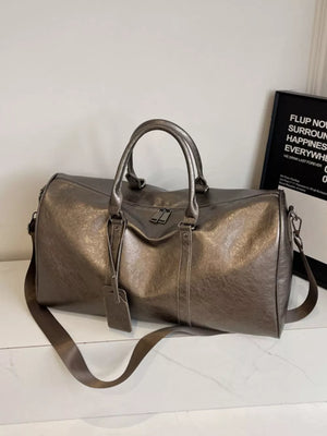 Textured metallic duffle bag in champagne color with detachable strap and luggage tag.