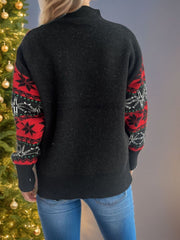 Black acrylic sweater with festive snowflake and star print on sleeves.