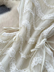 Tiered white lace midi dress with bow details and textured trim.