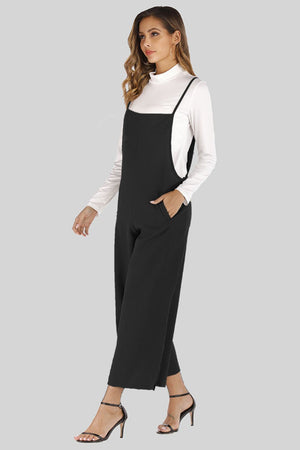 Black culotte overalls with slender straps and side pockets, worn over a white turtleneck.