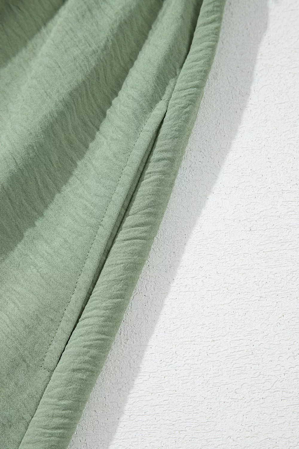 Sage green smocked mini dress detail showing textured fabric and seam.