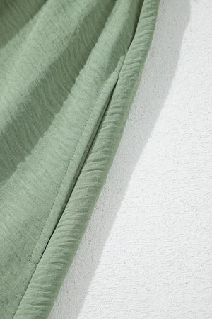Sage green smocked mini dress detail showing textured fabric and seam.