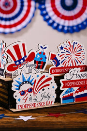 Patriotic wooden tabletop decor with USA flag hat, cupcake, fireworks, and Independence Day messages.