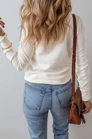 White long sleeve waffle knit blouse with a casual fit, styled with jeans and a crossbody bag.