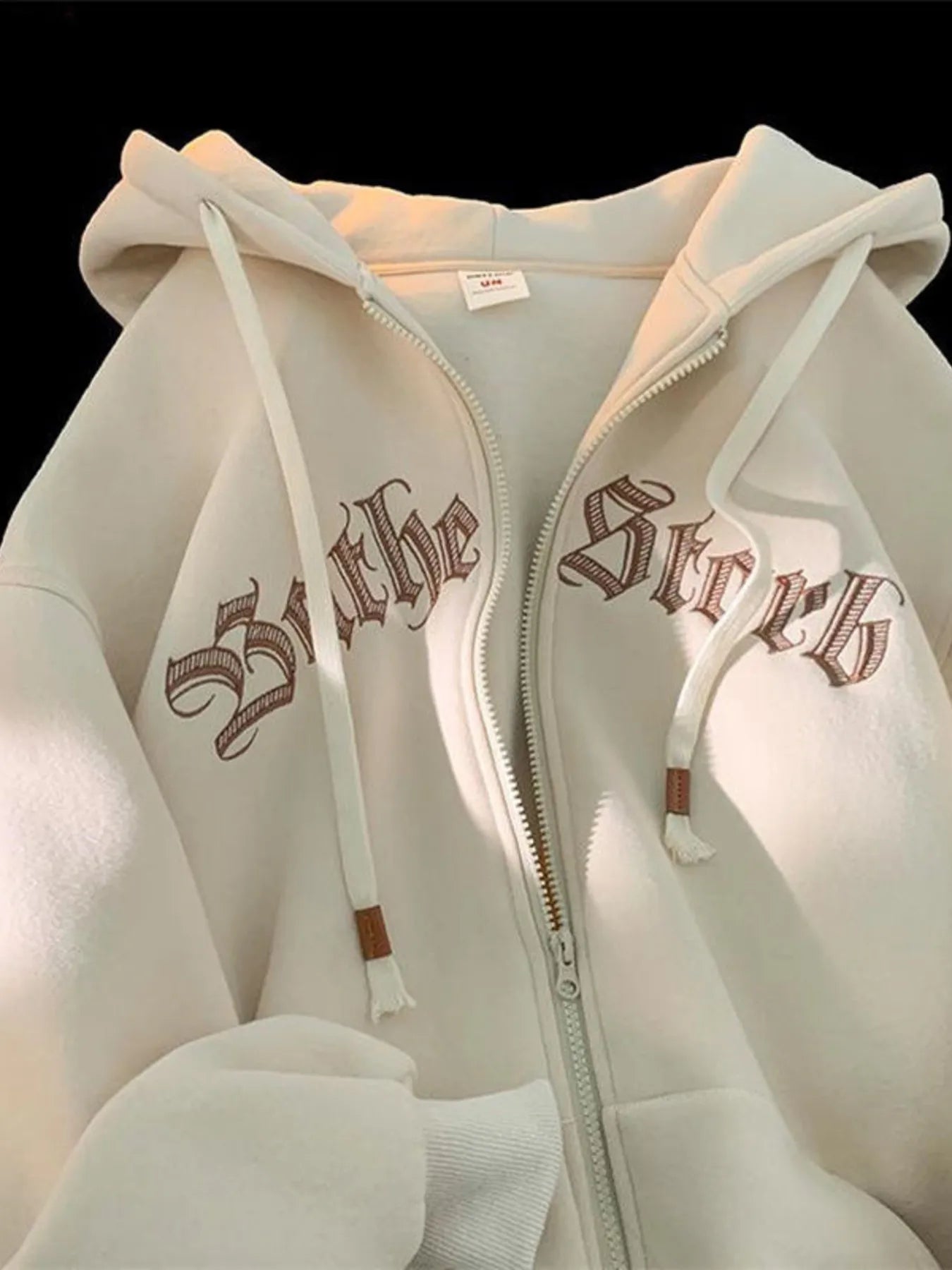 Apricot zip up hoodie with drawstring and gothic text graphic detail.