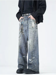 Men's wide-leg jeans in dusty blue denim with paint splatters and chain detail.