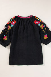 Black voluminous blouse with embroidered floral sleeves and pink scalloped neckline.