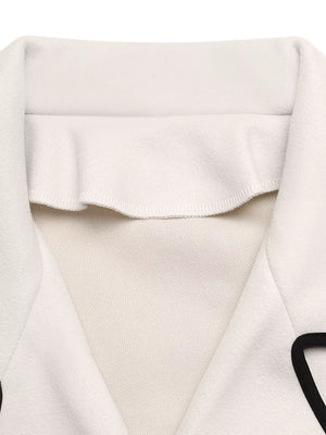 Beige bolero jacket with black contrast trim and ruffled neckline detail.