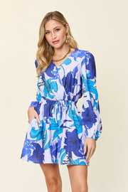 Blue floral wrap romper with long sleeves, V-neck, cinched waist, and pockets.