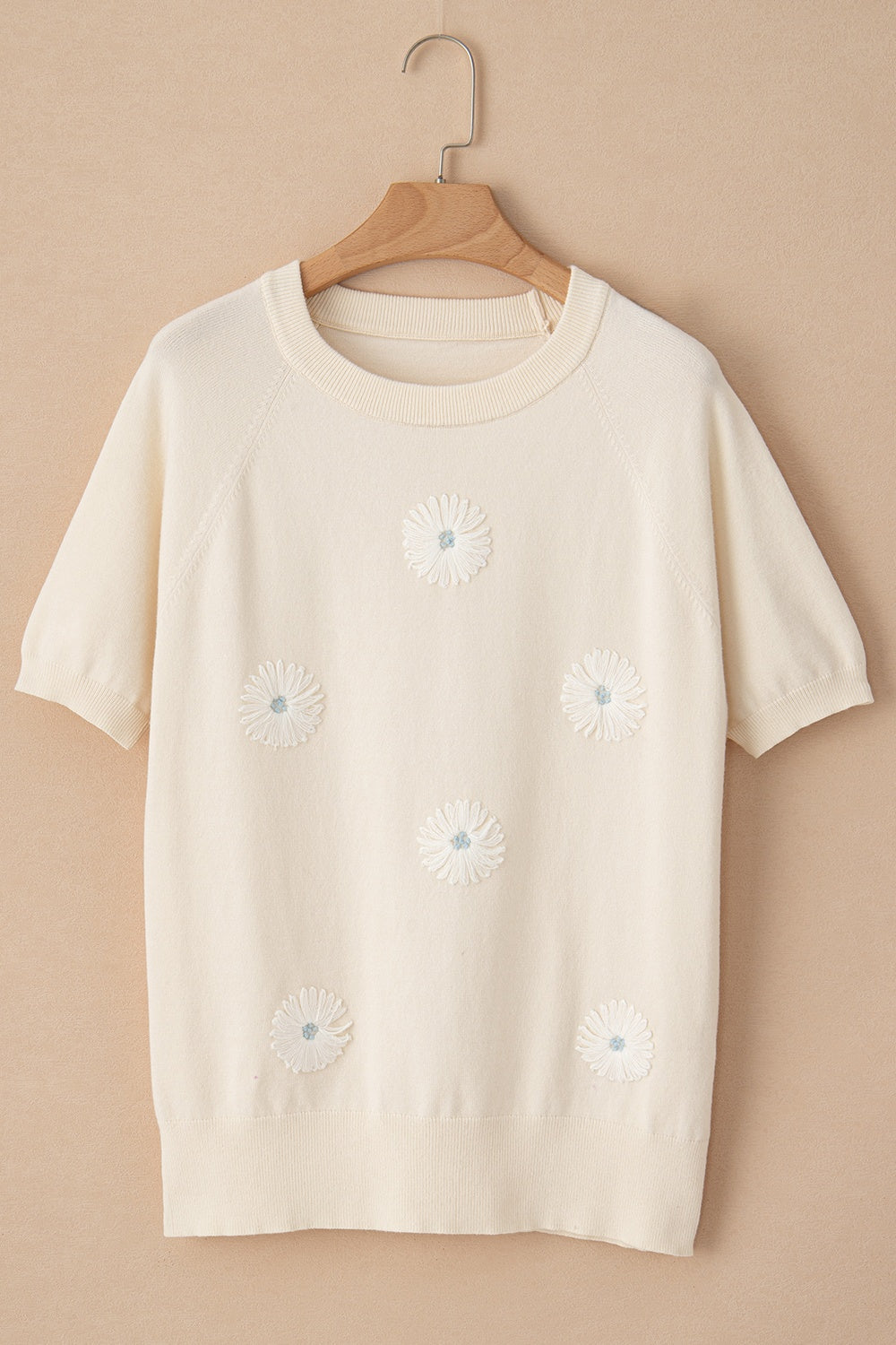 Ivory knit top with short sleeves and daisy appliqué details.