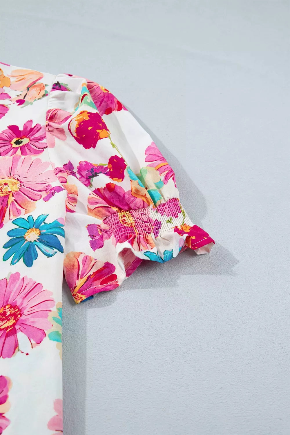 White cotton blouse with vibrant floral print, short ruffled sleeves with smocking detail.