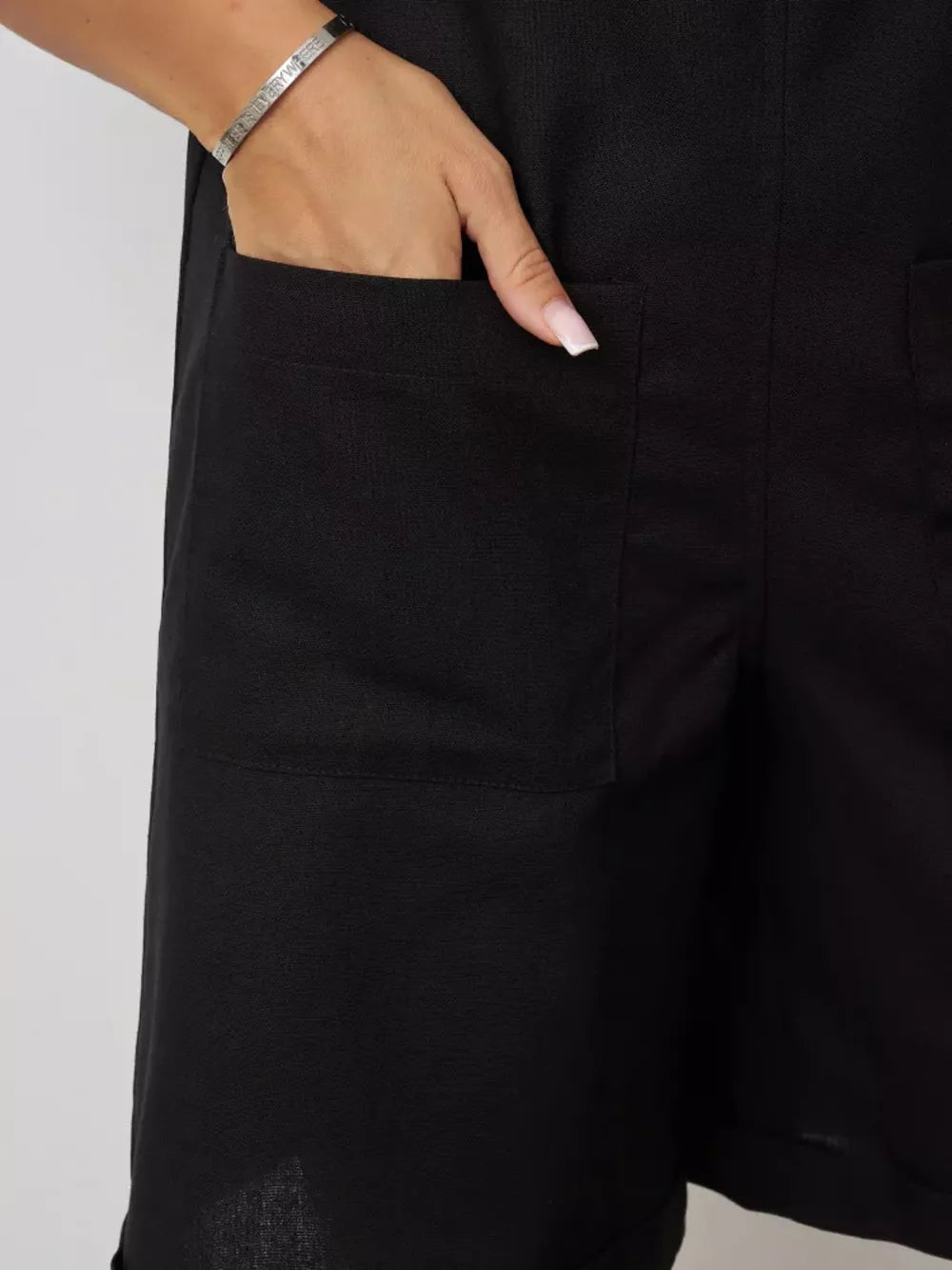 Black cotton romper with functional pockets and tie straps, close-up detail.