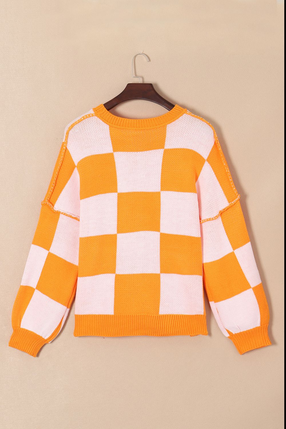 Checkerboard knit crewneck sweater in orange and white with balloon sleeves.