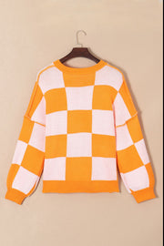 Checkerboard knit crewneck sweater in orange and white with balloon sleeves.