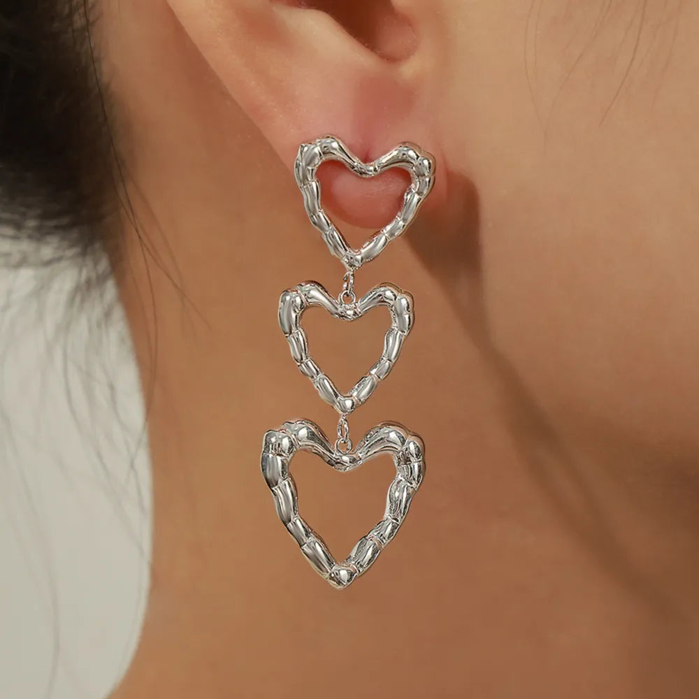 Silver triple heart drop earrings with textured detail.
