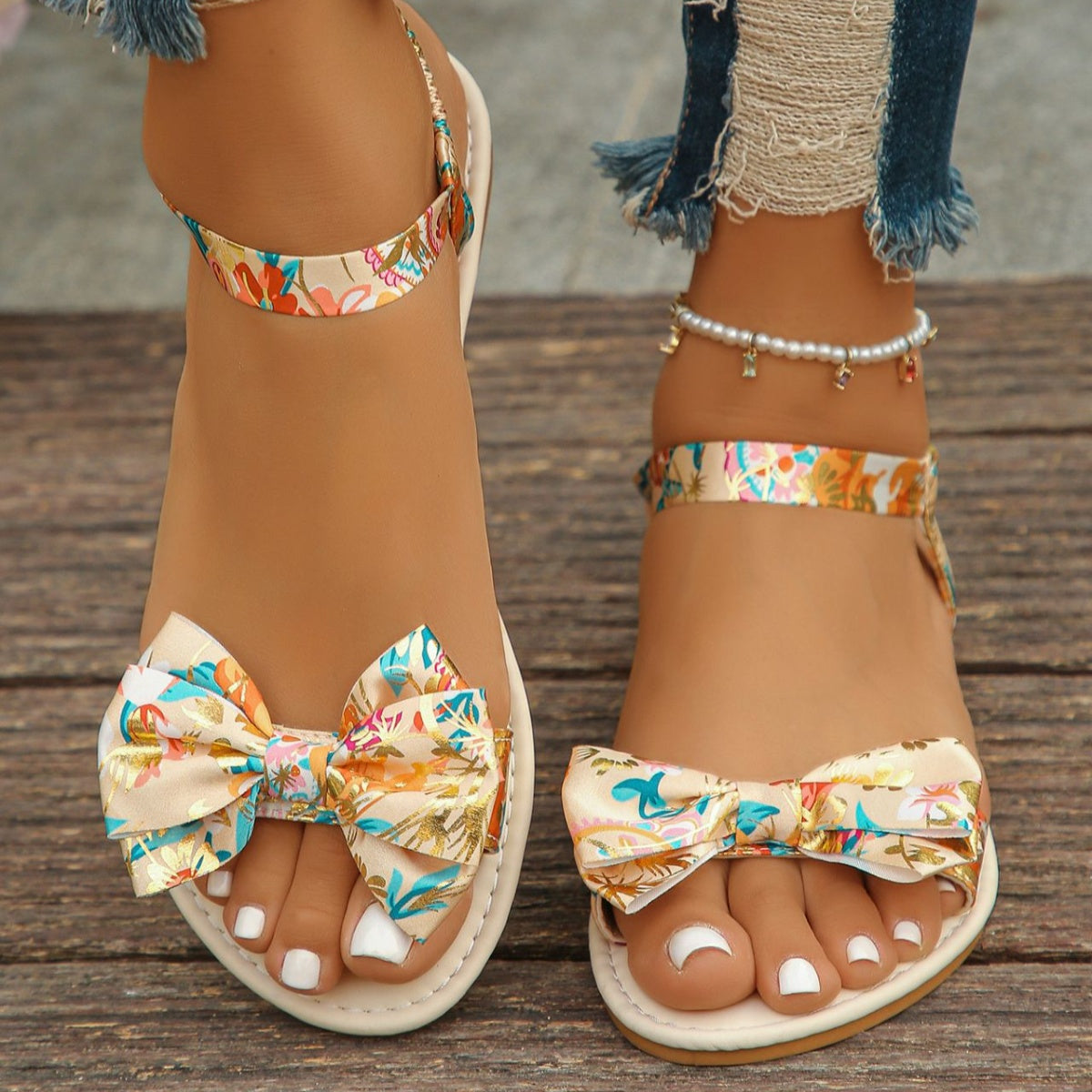 Beige flat sandals with floral print bowknot detail and ankle strap.