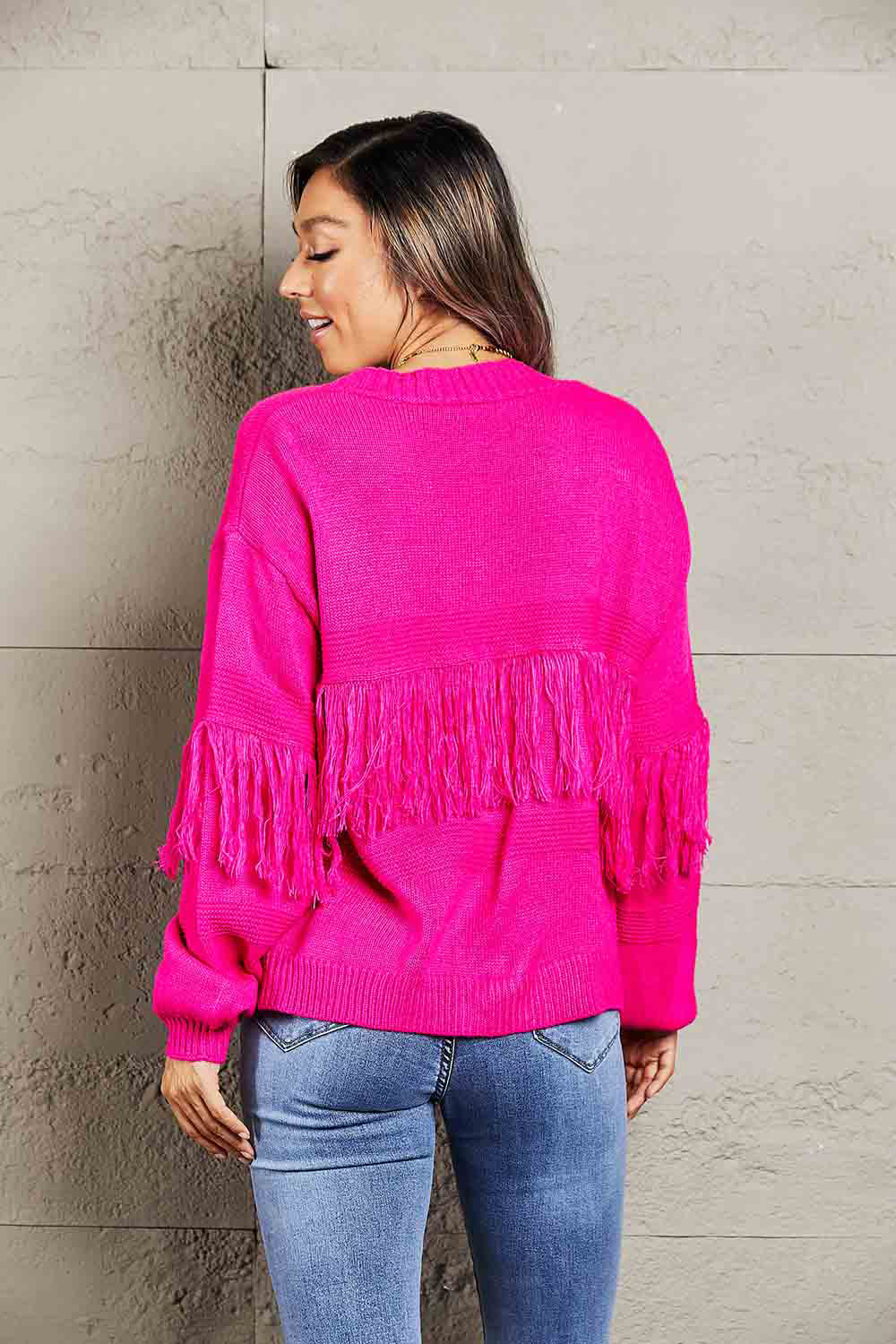 Hot pink acrylic cardigan with fringe detail on sleeves and back.