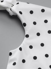 White polka dot mini dress with asymmetrical neckline and bow detail.