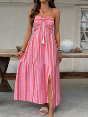 Pink halter neck midi dress with geometric pattern, tie front, tassel detail, and thigh slit.
