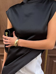 Black cap sleeve turtleneck blouse with asymmetrical hem and gold bracelet.