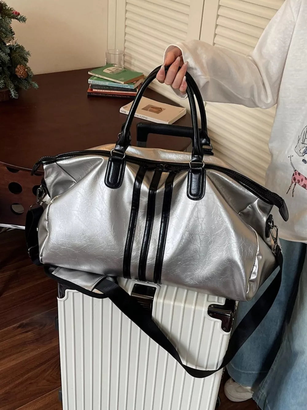 Sleek silver metallic duffle bag with black stripes and handles.