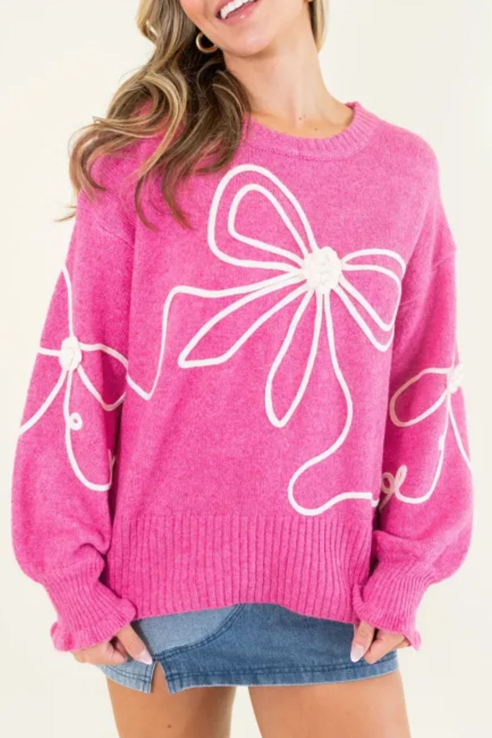 Fuchsia pink knit sweater with embroidered white bow motif and ribbed cuffs.
