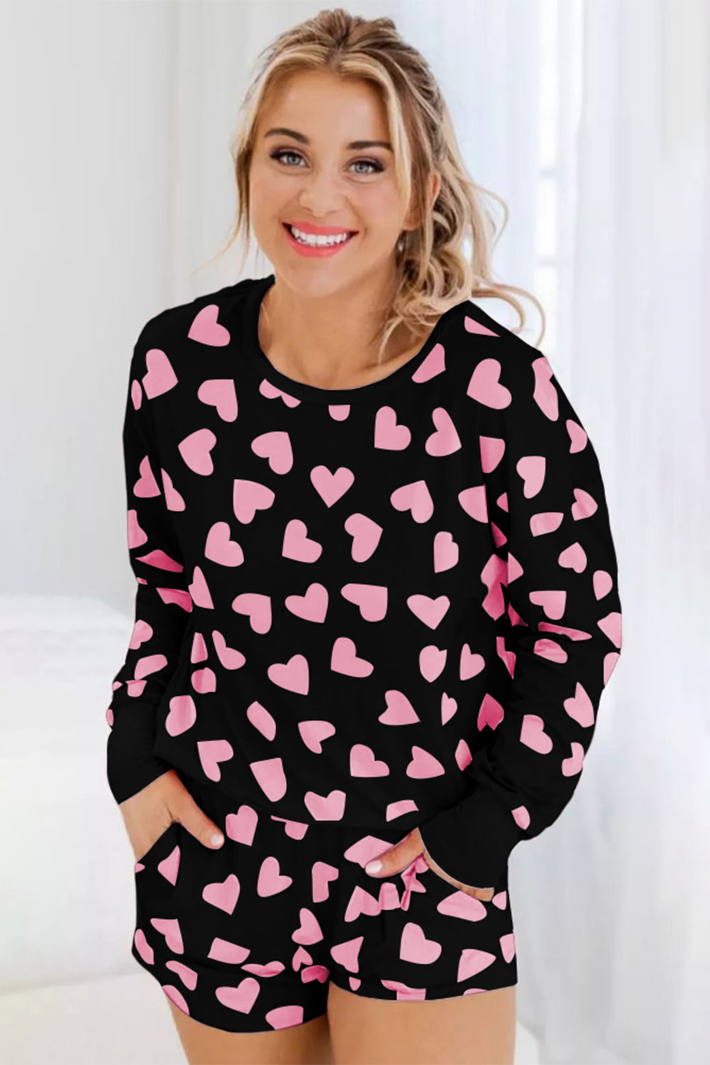 Black pajama set with pink heart print, long sleeves, crew neck, and shorts with pockets.