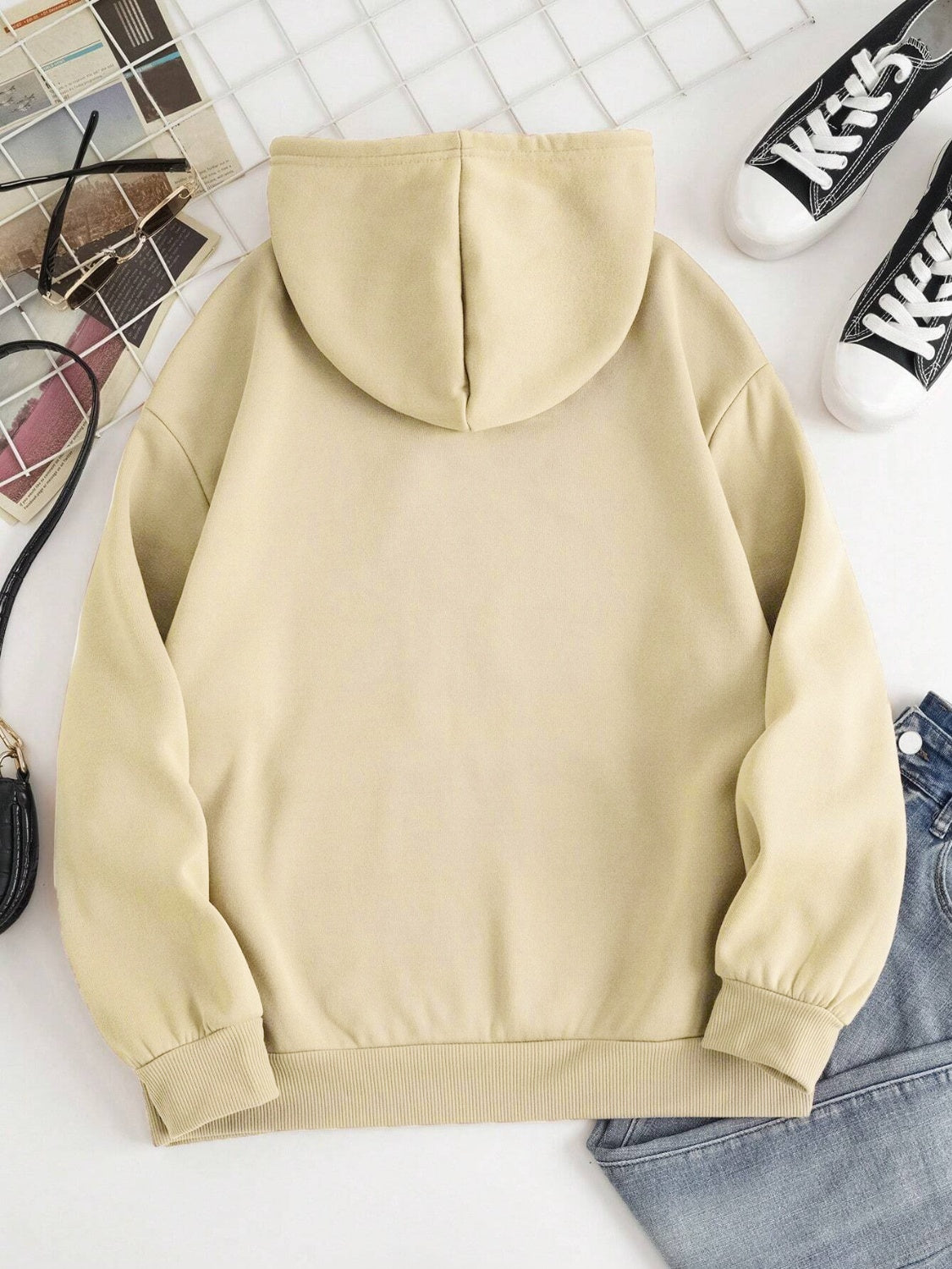 Oversized beige hoodie with pouch pocket and ribbed cuffs, styled with jeans and sneakers.