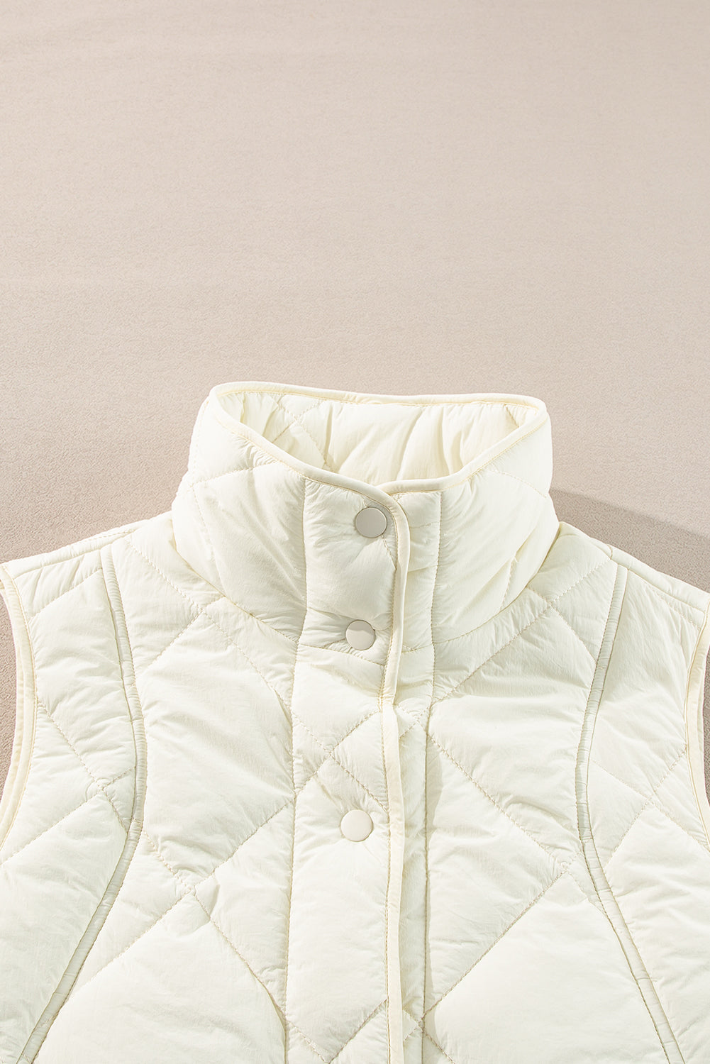 Ivory quilted stand collar vest with snap front closure and diamond pattern.