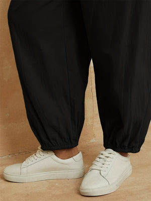 Black cotton overalls jumpsuit with cinched ankles, styled with white sneakers.