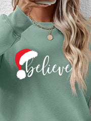 Sage raglan sweatshirt with white "believe" graphic and Santa hat detail.