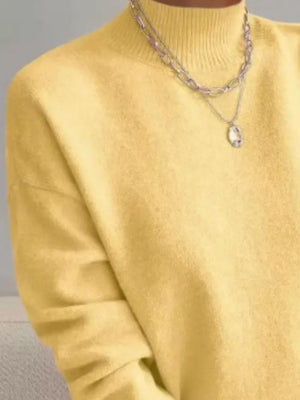 Light yellow mock neck knit sweater with dropped shoulders, styled with layered necklaces.
