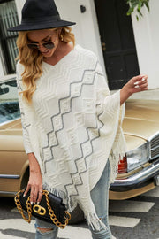 White knit poncho with geometric pattern, pearl embellishments, and fringe detail.