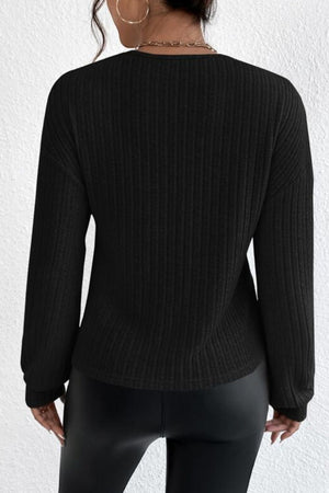 Black ribbed knit top with blouson sleeves and a cross-front detail, styled with faux leather pants.