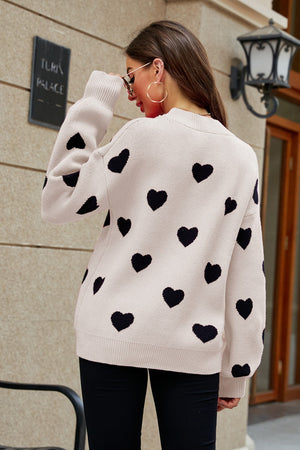 Beige knit sweater with black heart pattern, balloon sleeves and crew neck.