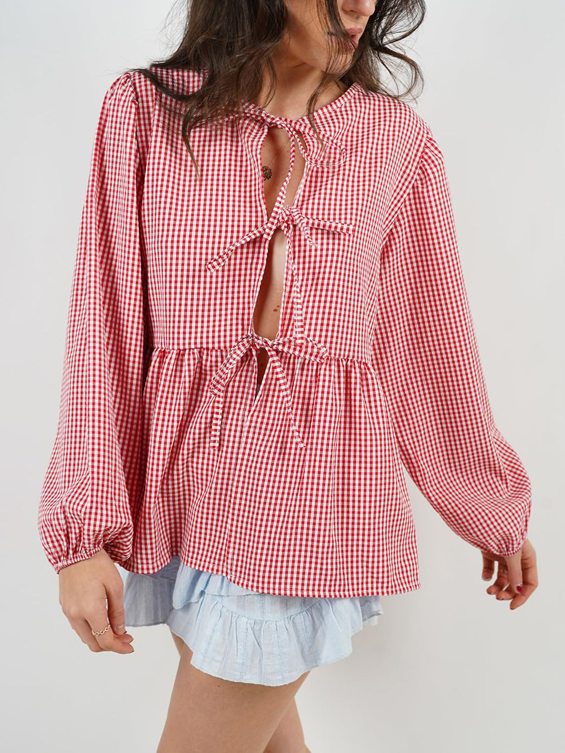 Red gingham tie-front peplum blouse with voluminous sleeves and a ruffled hem.