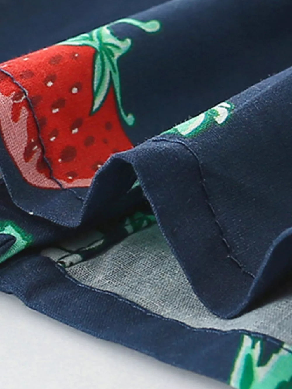 Navy cotton baby dress with allover red strawberry print and ruffle sleeve detail.