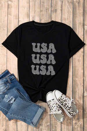 Black t-shirt with stacked rhinestone USA graphic and rolled sleeves.