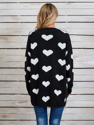 Black acrylic cardigan with white intarsia hearts, crew neck, long sleeves.