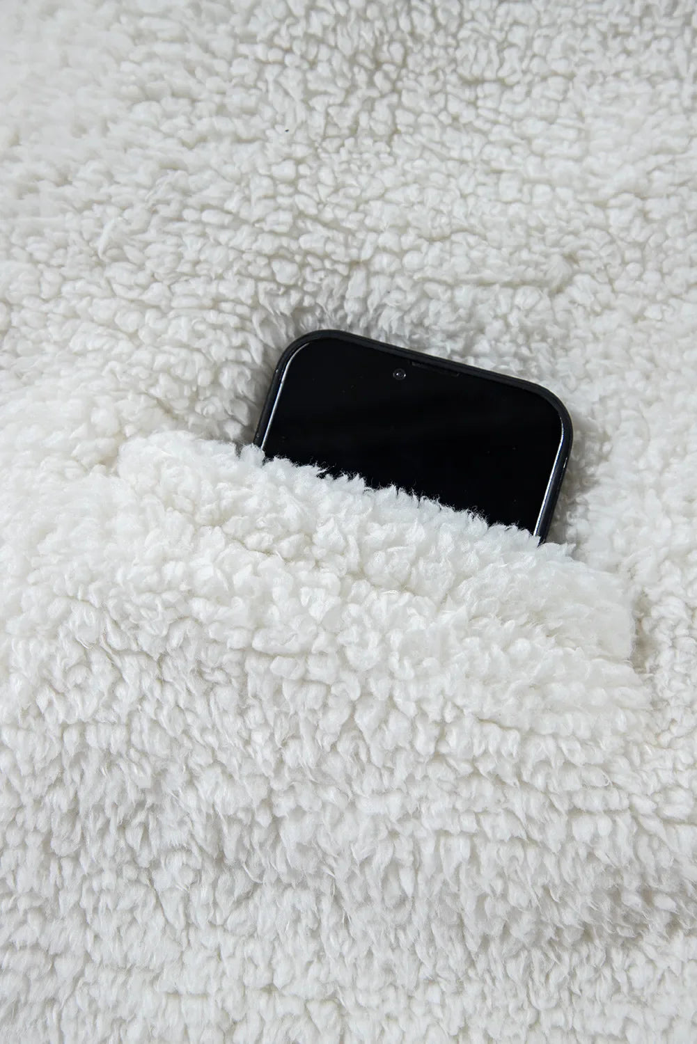 White teddy bear collarless jacket with a pocket holding a black smartphone.