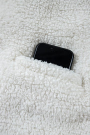 White teddy bear collarless jacket with a pocket holding a black smartphone.