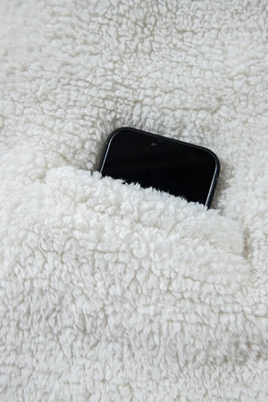 White teddy bear collarless jacket with a pocket holding a black smartphone.