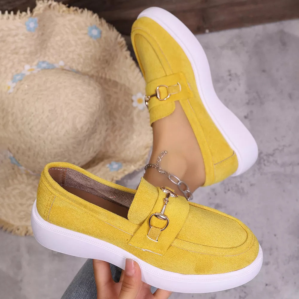 Yellow slip-on loafers with gold horse-bit detail and white soles, styled with a straw hat.