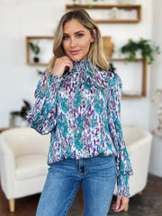 High neck abstract print blouse with smocked cuffs and neckline in blue, purple, and white.